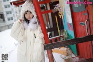 A woman in a white coat leaning against a tree.