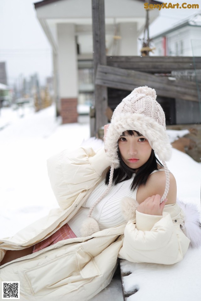 A woman sitting on a bench in the snow wearing a hat.