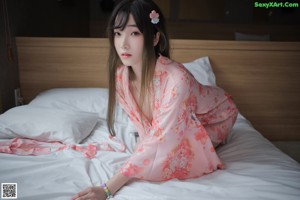 A woman in a pink kimono laying on a bed holding a fan.