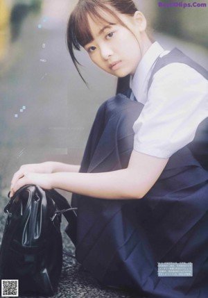 A young woman in a school uniform sitting on the floor.