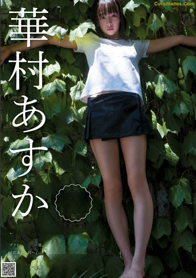 A woman in a white shirt and black skirt posing in front of ivy.