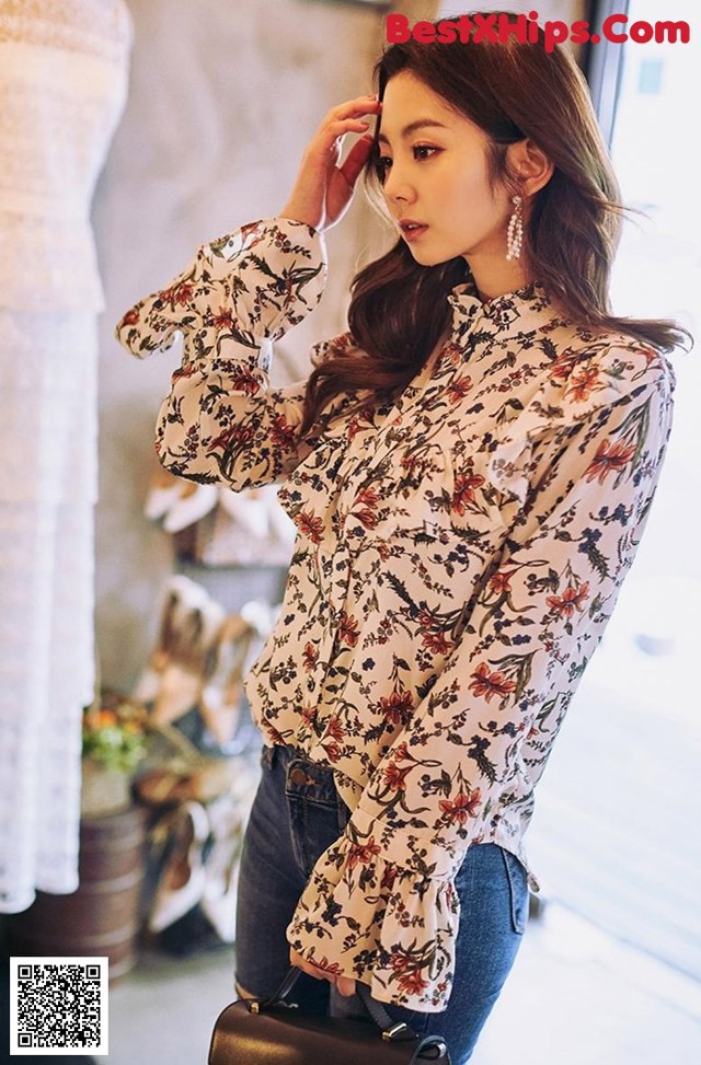 a woman wearing a white blouse and jeans standing in front of a window