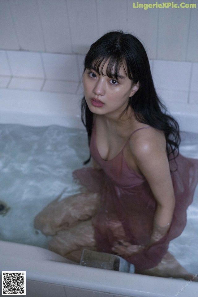 A woman in a pink dress sitting in a bathtub.