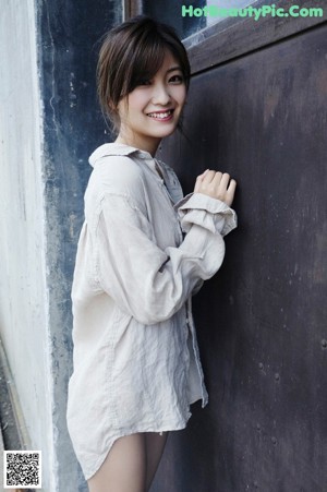 A woman in a white dress leaning against a wall.