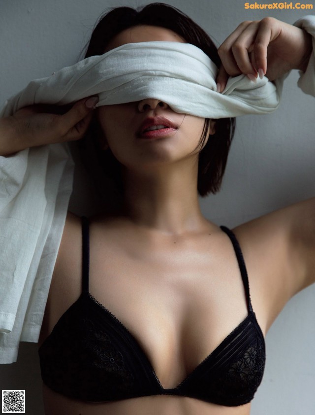 A woman in a black bra with a white sheet covering her eyes.