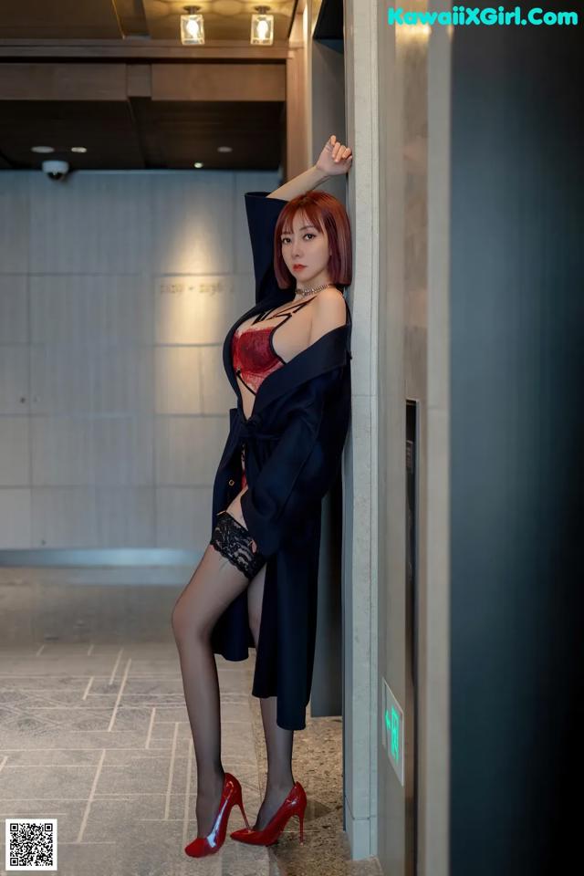 A woman in a black robe and red high heels leaning against a wall.