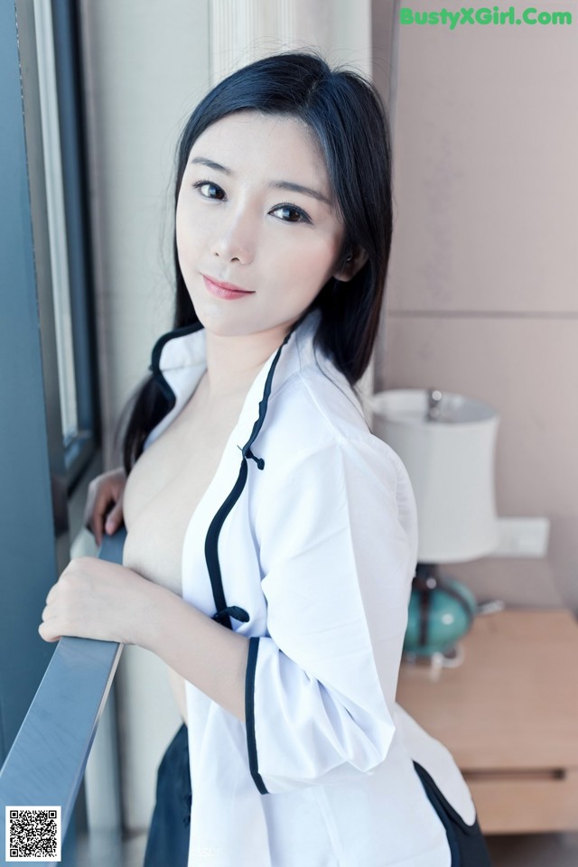 A woman in a white shirt and black skirt leaning against a window.