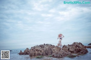 A woman with pink hair sitting on a rock by the ocean.