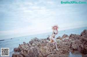 A woman with pink hair wearing a straw hat on the beach.
