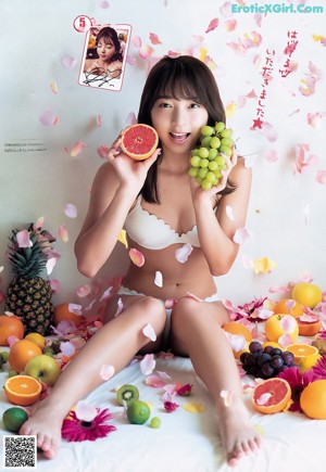 A woman laying on a bed covered in fruit and flowers.