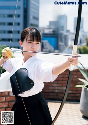 A woman in a white shirt and black skirt holding a bow and arrow.