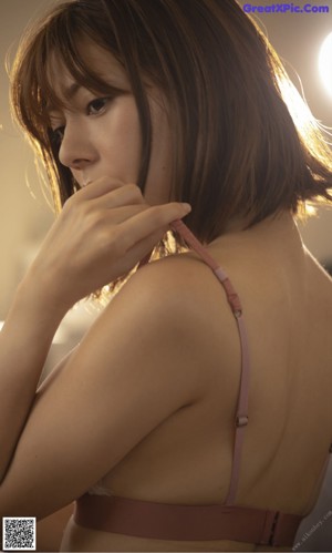 A woman in a white bra top sitting on a bed.