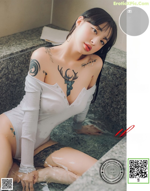 A woman with a tattoo on her arm sitting in a bathtub.