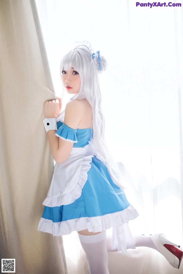 A woman in a blue and white dress leaning against a curtain.