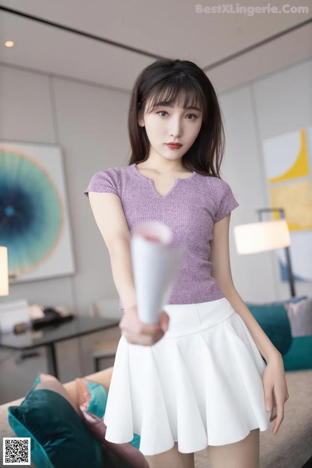 A woman in a purple top and white skirt holding a white object.