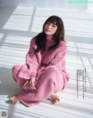 A woman in a pink sweater sitting on the floor.