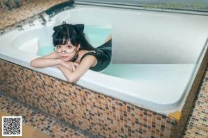 A woman in a black bathing suit sitting in a bathtub.