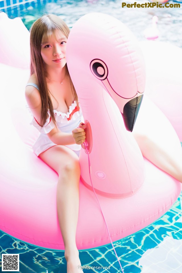 A young girl sitting on an inflatable flamingo in a pool.