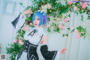 A woman dressed in a maid outfit standing in front of flowers.