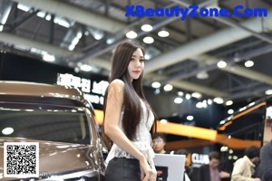 A woman standing next to a black car at a car show.