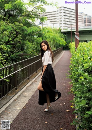 A woman in a black dress leaning on a railing by the water.