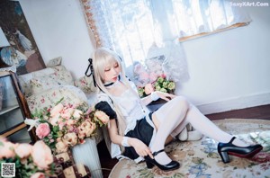 A woman in a maid outfit sitting on a bed.