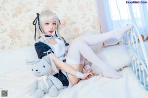 A woman in a maid outfit sitting on a bed with a stuffed animal.