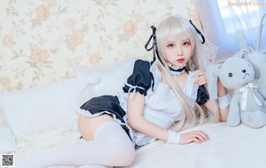 A woman in a maid outfit sitting on a bed with a stuffed animal.