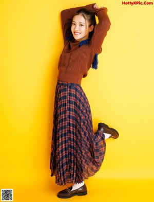 A woman in a brown sweater and blue scarf smiles at the camera.