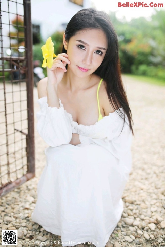 A woman in a white dress holding a yellow flower.