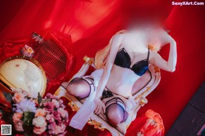 A woman laying on a red bed next to a birdcage.