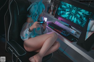 A woman with blue hair sitting on a chair in front of a computer.