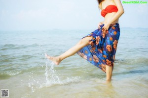A woman in a red bikini sitting on a blue and white checkered blanket.