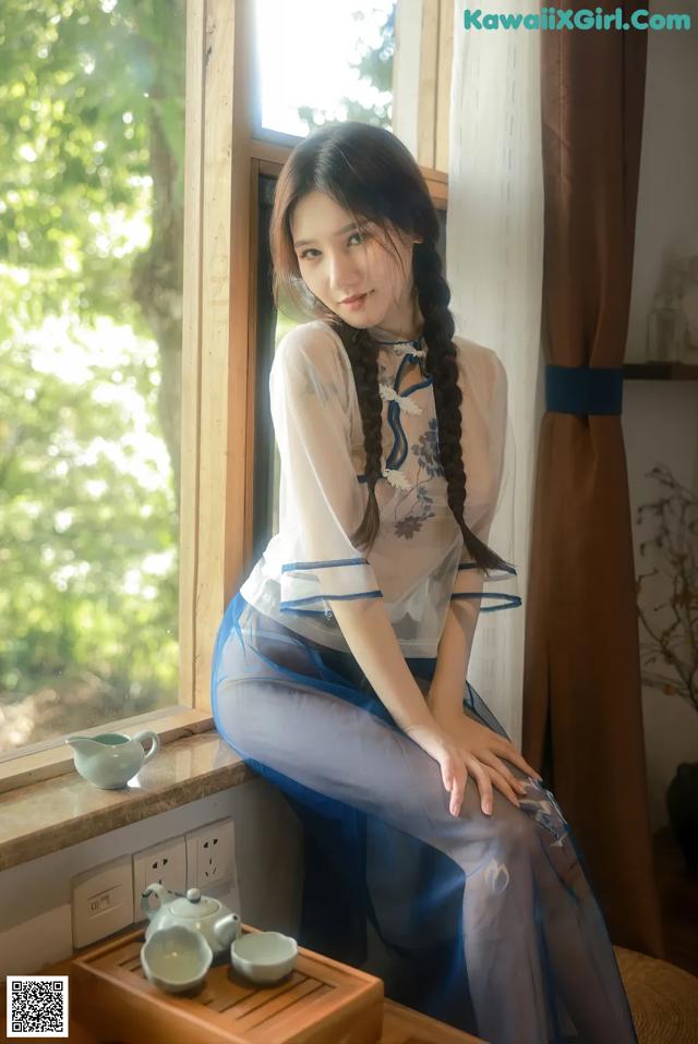 A woman sitting on a window sill next to a window.