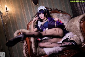 A woman in a maid outfit sitting on a couch.