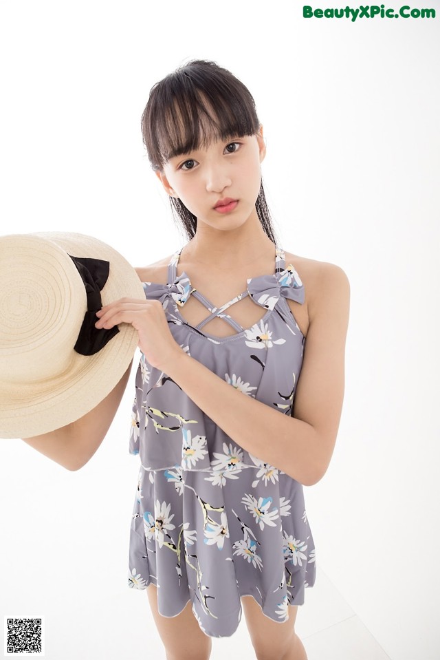 A woman in a gray dress holding a straw hat.