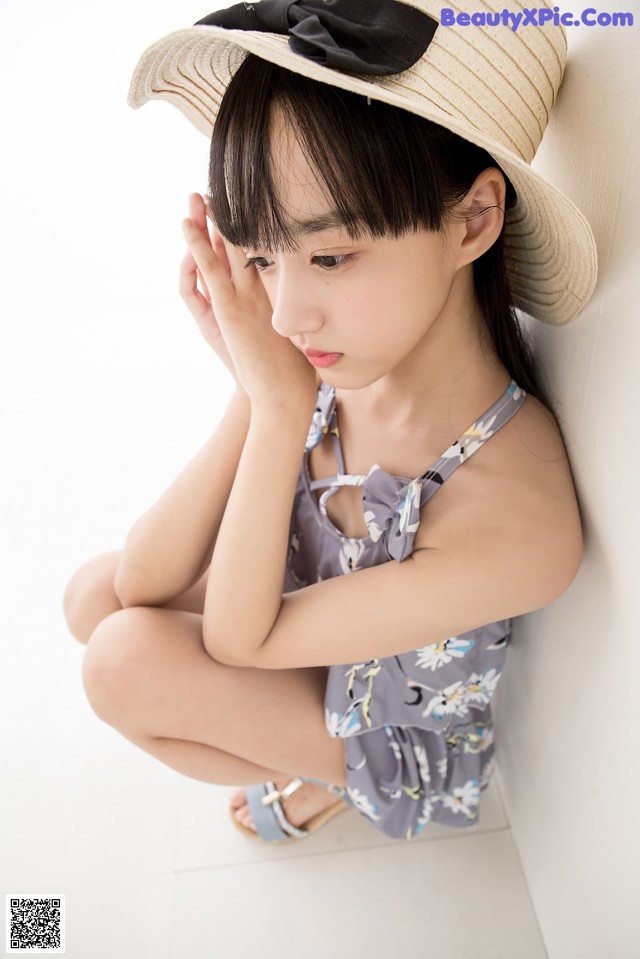 A little girl wearing a straw hat sitting on the floor.