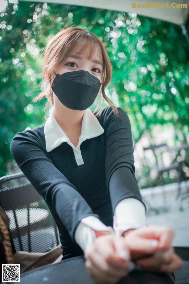 A woman wearing a black face mask sitting at a table.