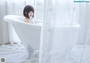 A woman in a white dress sitting in a bathtub.