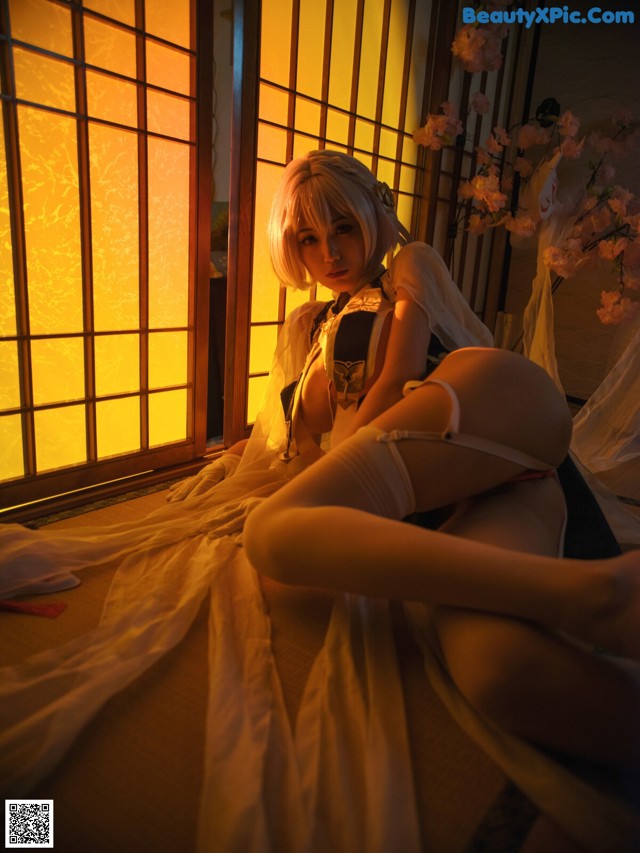 A woman in lingerie sitting on a bed in front of a window.