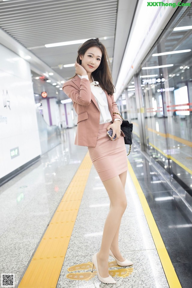 A woman in a pink skirt and a pink blazer posing for a picture.